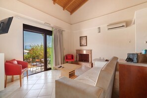 A living room with a sofa, a red chair, a table, a fireplace, and a sliding glass door leading to an outdoor area. - Villa 'Fedra' with Balcony and Air Conditioning (Marathiás)