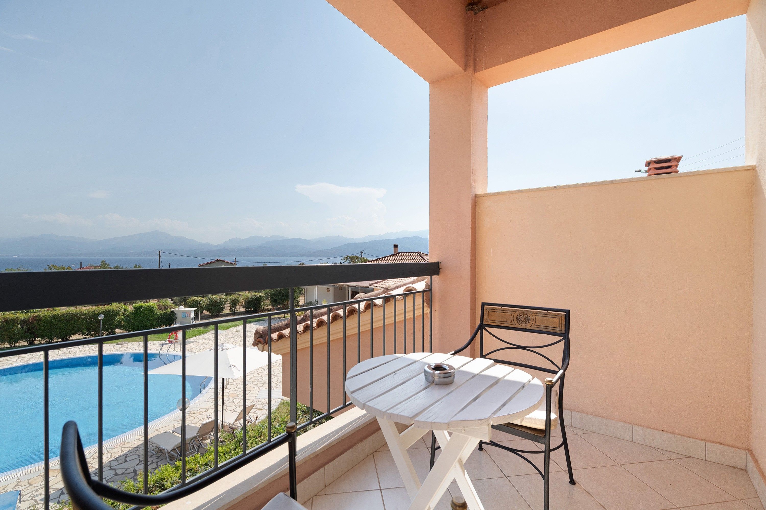 A balcony with a pool, a table, and chairs, overlooking a mountainous landscape.