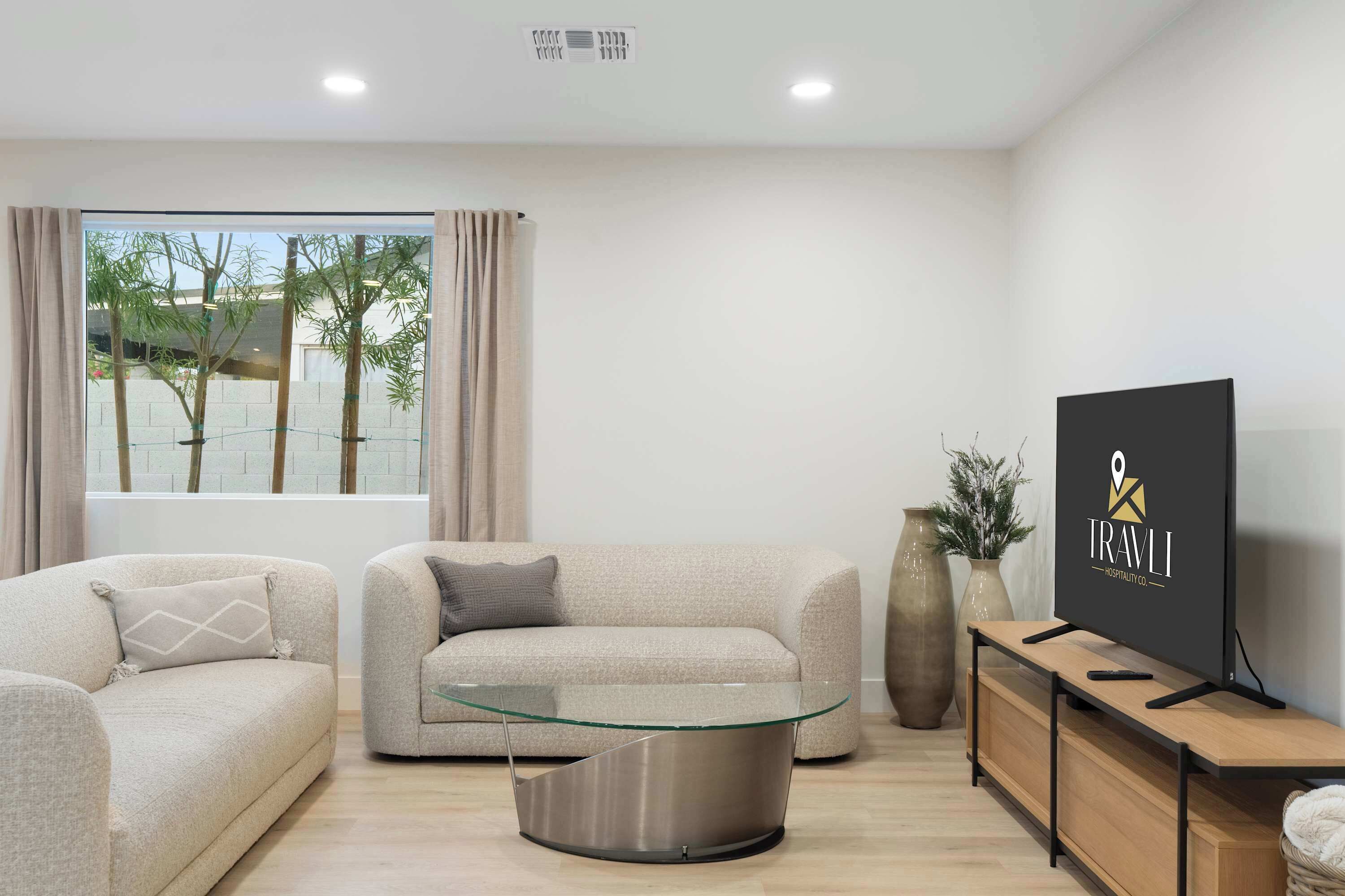 Een moderne woonkamer met een bank, fauteuil, glazen salontafel en een televisie op een houten dressoir.