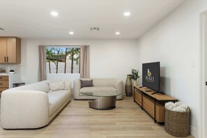 A modern living room with a sofa, a glass coffee table, a TV on a wooden stand, and a wicker basket. - NEW|The Belmont @ Kierland |Updated Oasis w/Pool (Scottsdale)