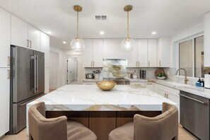 A modern kitchen with a marble island, stainless steel appliances, pendant lighting, and a central island with a gold bowl. - NEW|The Hawthorne @ Kierland|Pool & Putting Green (Scottsdale)