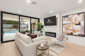 A modern living room with a white sofa, a glass coffee table, and a fireplace. There is a large window overlooking a pool and garden. - NEW|The Hawthorne @ Kierland|Pool & Putting Green (Scottsdale)