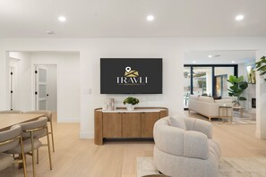 Ein modernes Wohnzimmer mit einem flachbildfernseher an der Wand, einem Essbereich mit Holztisch und Stühlen sowie einer Sitzecke mit Sofa und Pflanze.