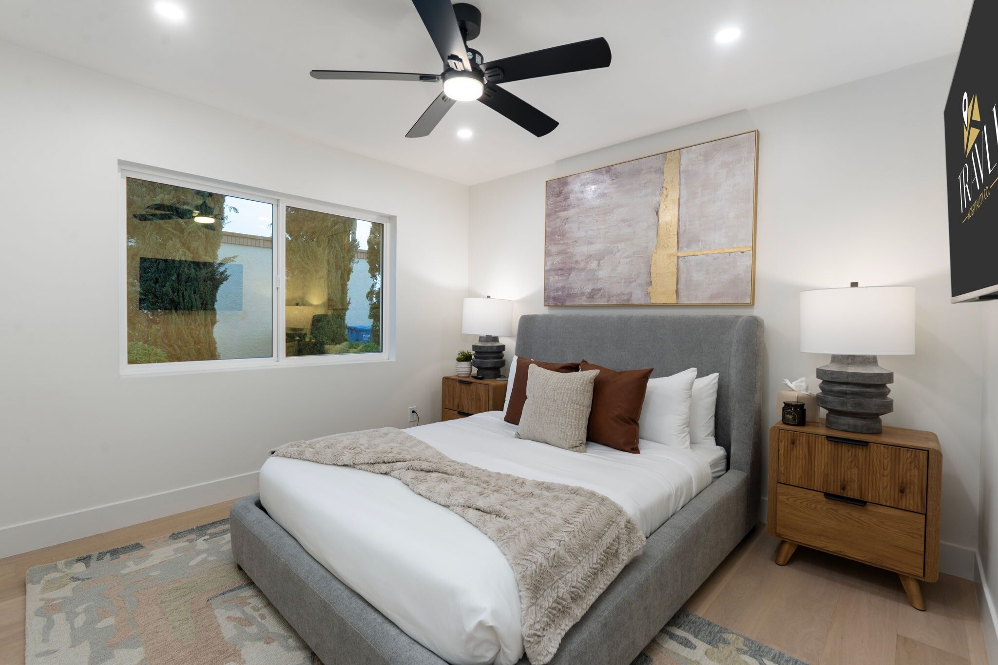 A bedroom with a bed, a ceiling fan, a window, and a bedside table.