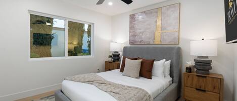 A bedroom with a bed, a ceiling fan, a window, and a bedside table.