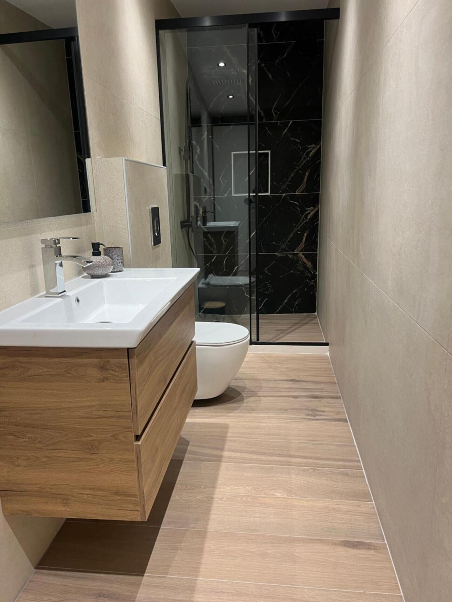 Een moderne badkamer met een houten wastafelmeubel, een wit toilet en een douchecabine met glazen wanden.