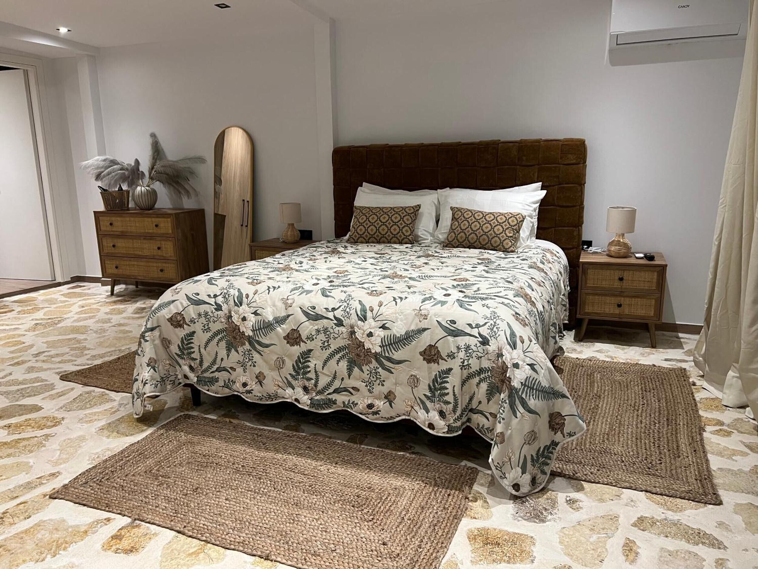 Ein Schlafzimmer mit einem großen Bett, zwei Nachttischen, einem Spiegel und einer Tür.