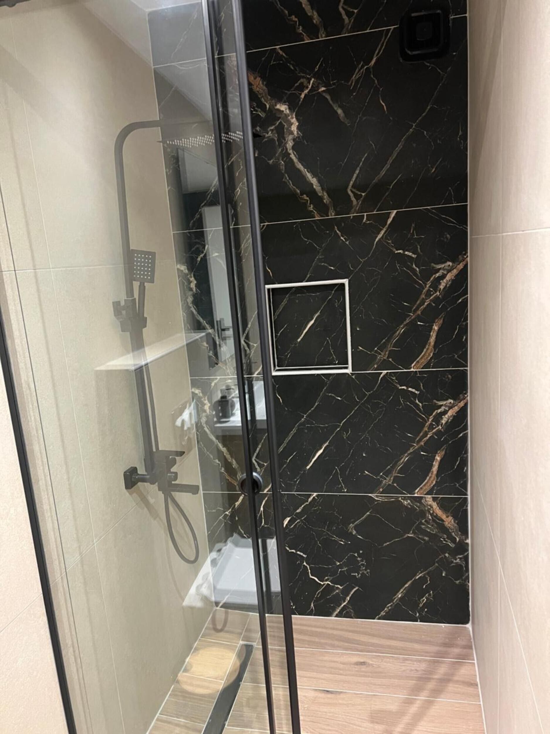 A glass-enclosed shower with a handheld showerhead and a wall-mounted control panel.