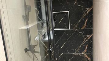 A glass-enclosed shower with a handheld showerhead and a wall-mounted control panel.