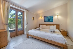 Quarto com cama, mesa de cabeceira, luminária na parede, pintura e vista através de uma porta de vidro.