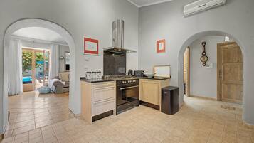 Una cucina moderna con isola centrale, forno integrato e piano cottura. Sono presenti due archi che conducono a una zona living con divano e finestra.
