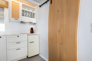 A kitchen with white cabinets, a small refrigerator, and a wooden door.