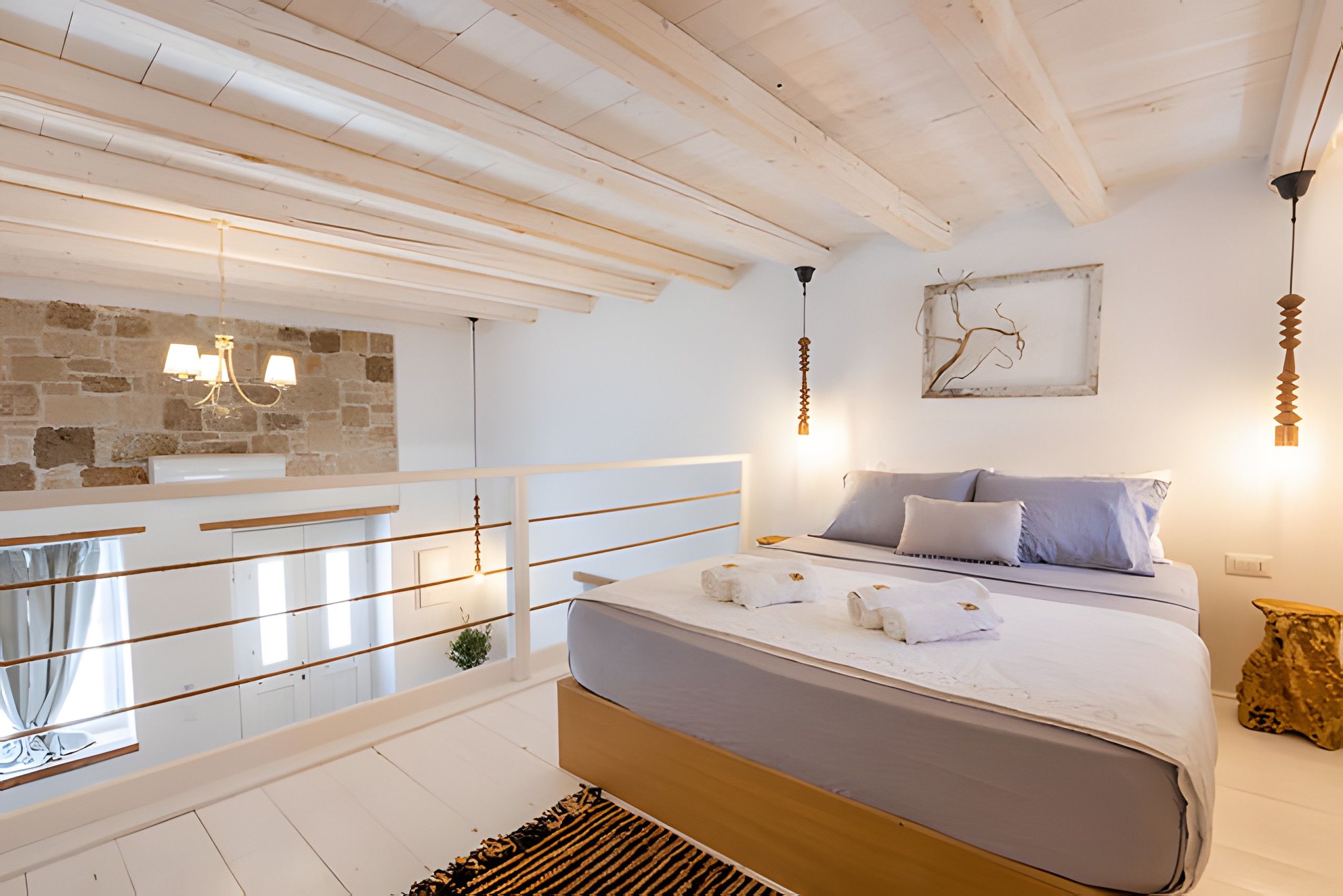 Een slaapkamer met een bed, een stenen muur, een balkon en een hanglamp.