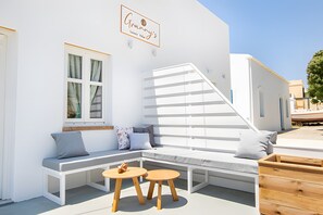 A white building with a sign reading 'Granny's' above a window. There is a white bench with cushions, a small table, and a wooden bench.