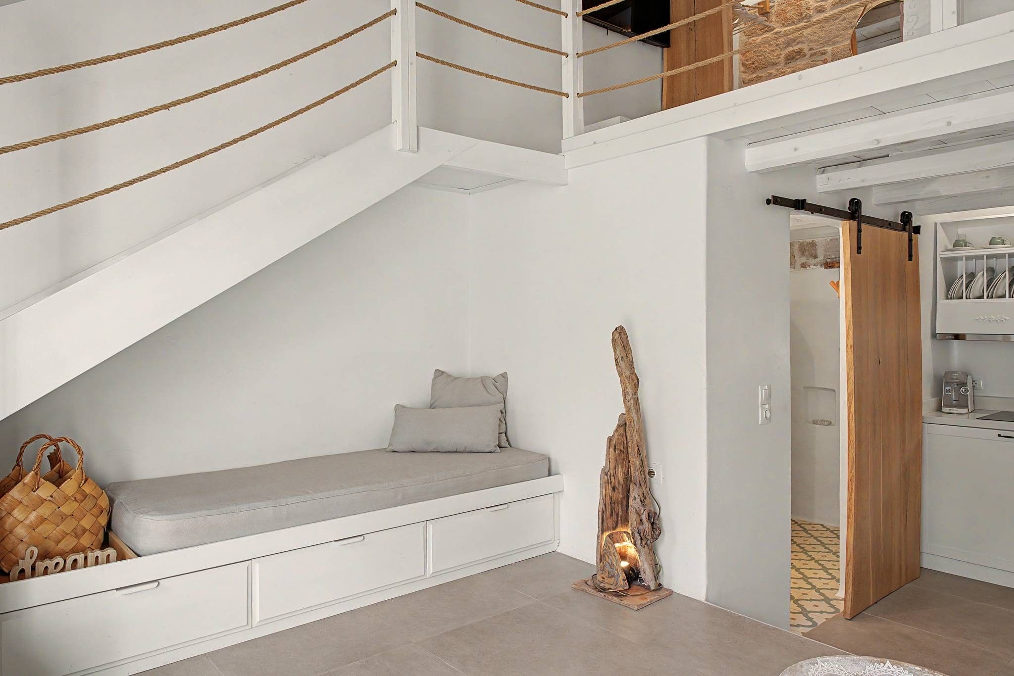 A loft-style room with a built-in bench, a wooden sculpture, and a kitchen area with a hanging rack.