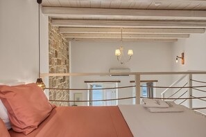 A bedroom with a bed, a stone wall, a wooden ceiling, a chandelier, a balcony railing, and a view of the sea. - Villa 'Grannys Finiki' with Mountain View, Wi-Fi and Air Conditioning (Karpathos)