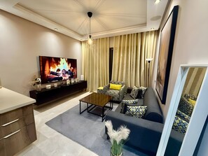 Ein modernes Wohnzimmer mit Flachbildfernseher, Sofa, Couchtisch und dekorativen Kissen.