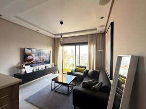 A modern living room with a flat-screen TV, a sofa, a coffee table, and a dining area. - Cozy 1-bedroom studio in charming Casablanca with AC (Casablanca)