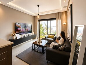 A modern living room with a flat-screen TV, a sofa, a coffee table, and a view of the city through large windows. - Cozy 1-bedroom studio in charming Casablanca with AC (Casablanca)