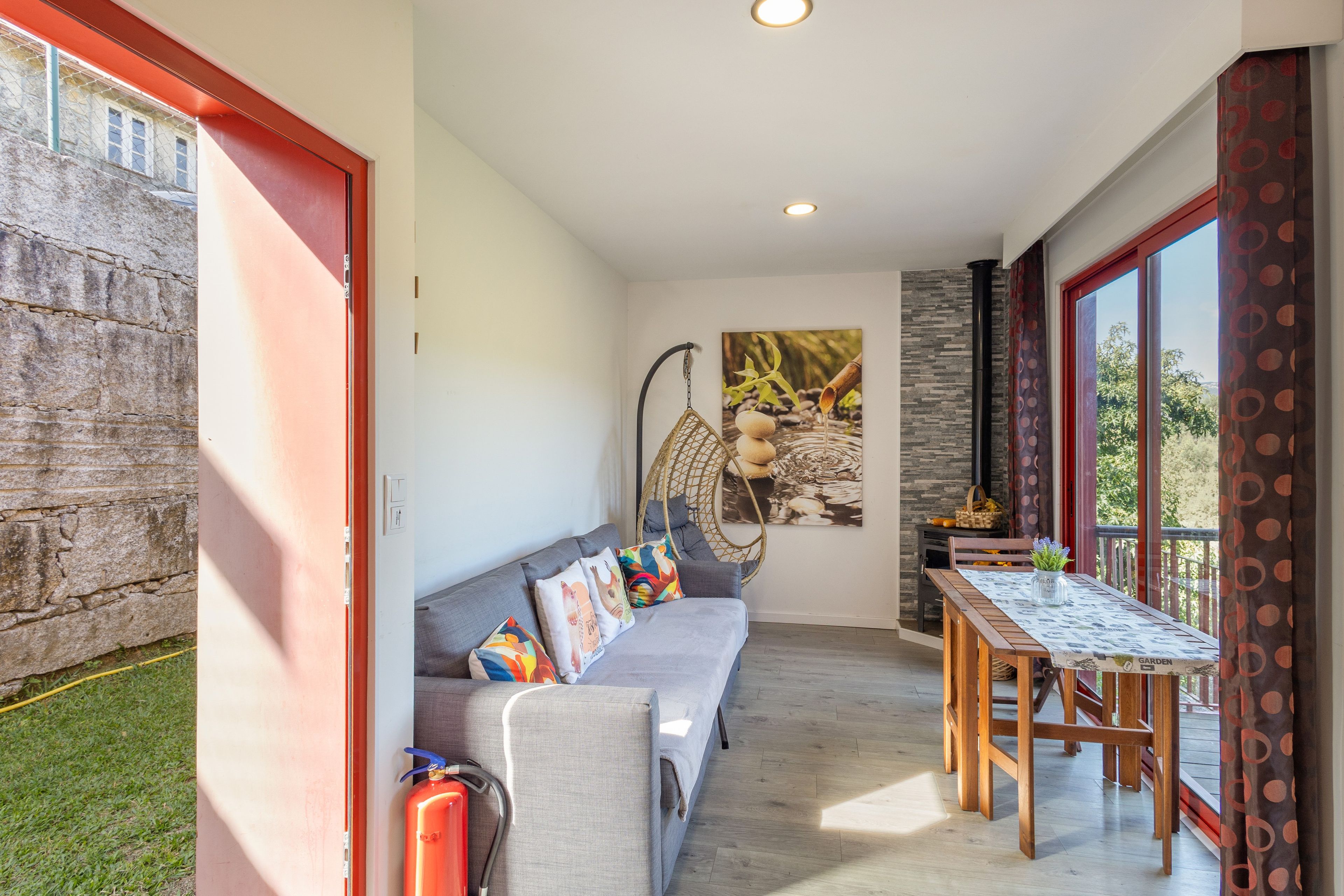 Un interior moderno con un sofá gris, un sillón colgante, una mesa de comedor y un amplio ventanal.