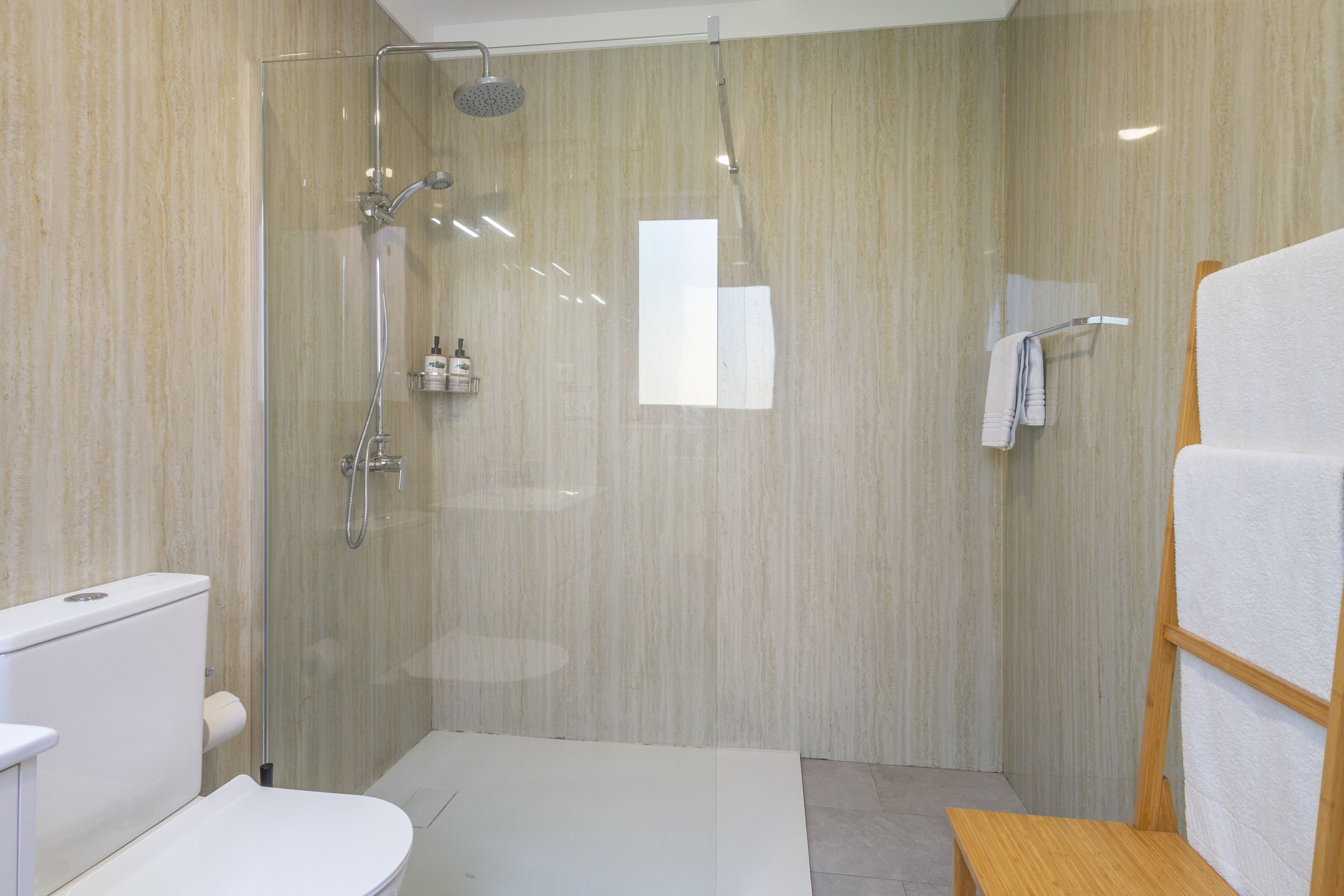 A modern bathroom with a glass-enclosed shower, a toilet, and a wooden bench.
