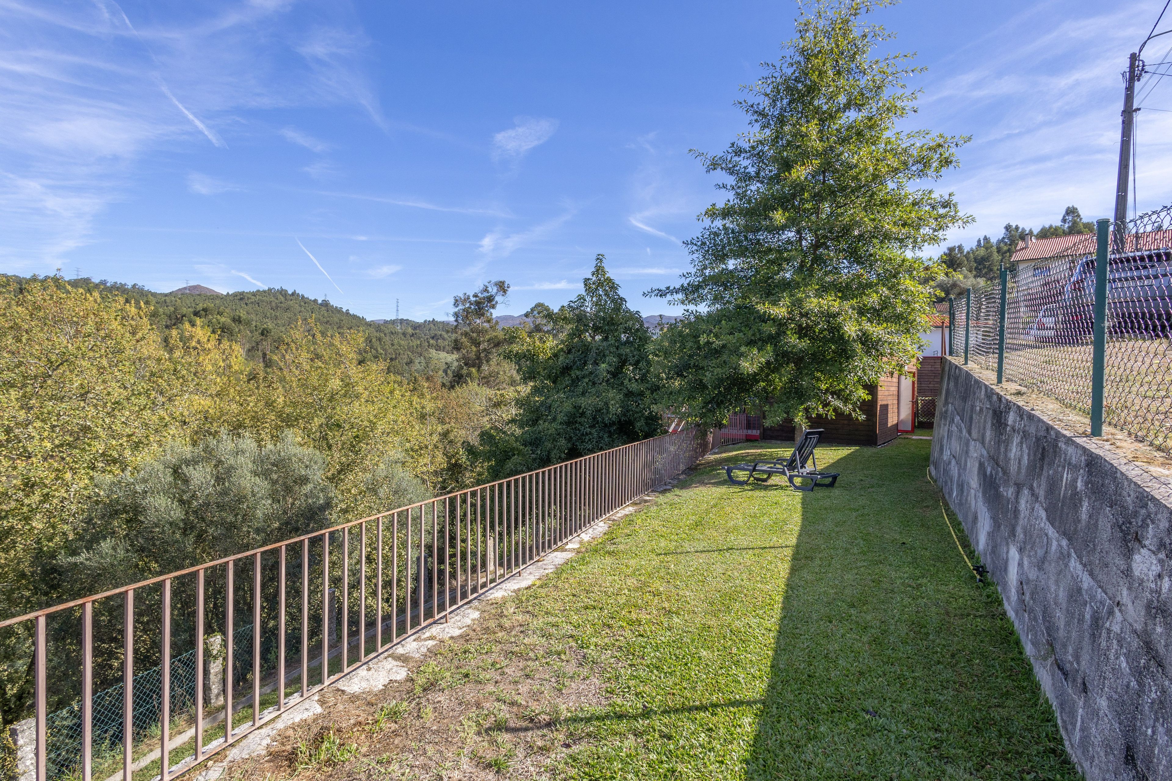 Un espace extérieur clos, avec une pelouse verdoyante, un banc et une vue sur une colline boisée.