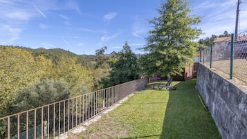 Un espace extérieur clos, avec une pelouse verdoyante, un banc et une vue sur une colline boisée.