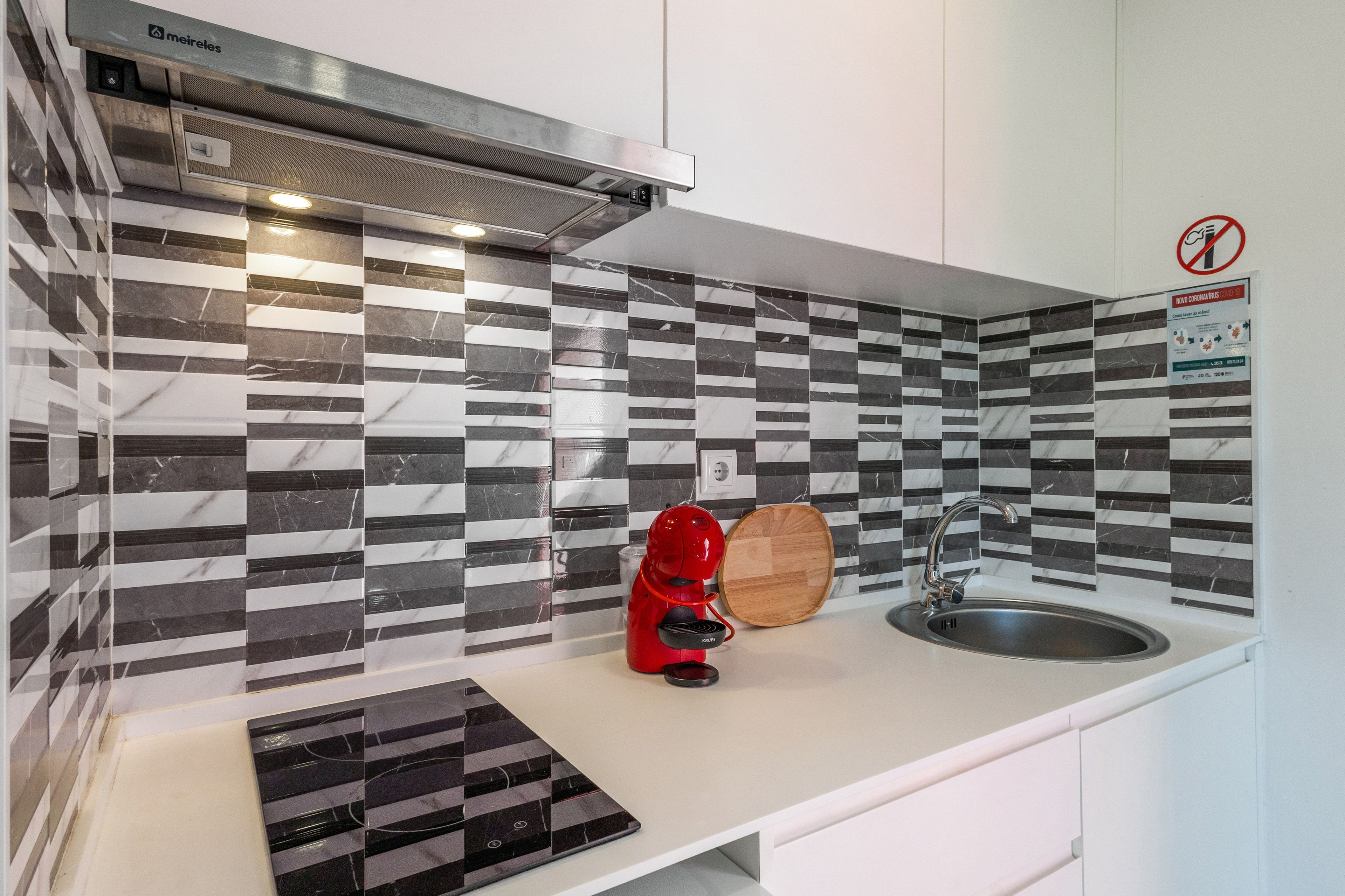 Une cuisine moderne avec un crédence à carreaux noirs et blancs, une machine à café rouge et un évier en acier inoxydable.