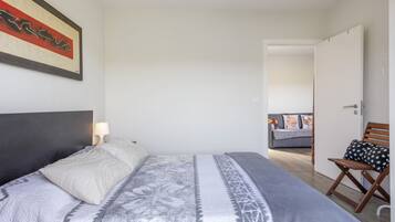 A bedroom with a bed, a nightstand, a lamp, a chair, and a door leading to another room.