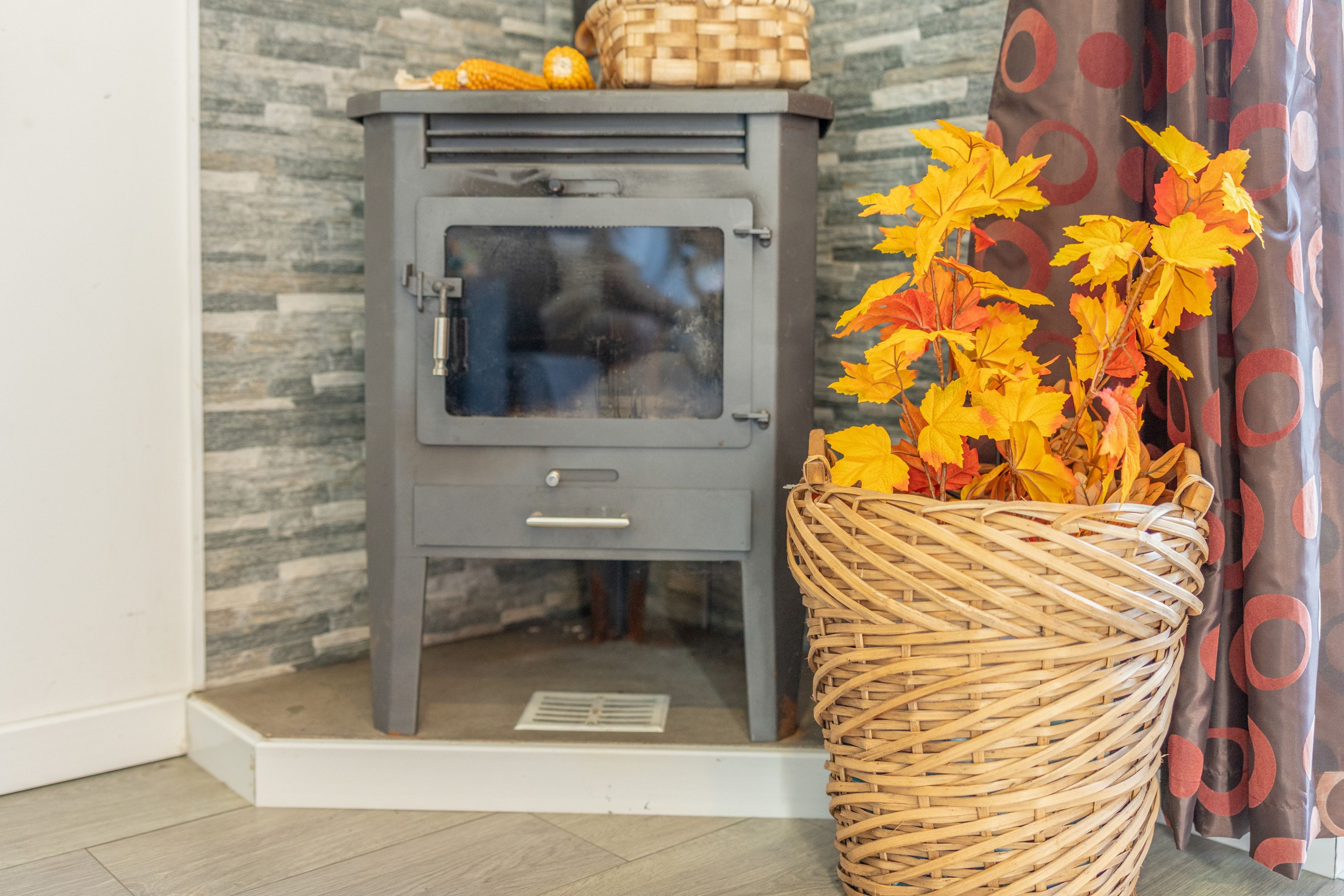 A corner room with a grey cabinet, a wicker basket with autumn leaves, and a patterned curtain.