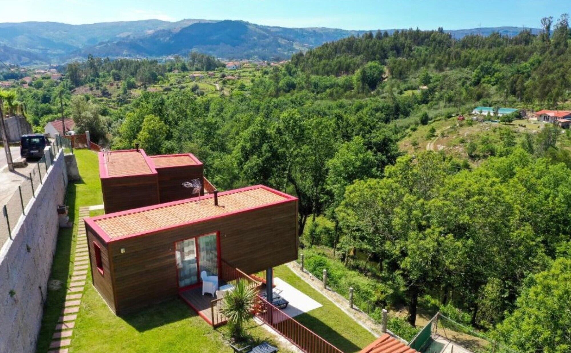Eine moderne Holzhütte mit zwei Stockwerken, einem roten Dach, einem Glastür-Eingang und einer kleinen Terrasse.