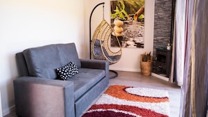 A modern living room with a grey sofa, a hanging chair, a rug, and a fireplace. - Bungalow 'Casinhas Do Minho' with Lake View, Wi-Fi and Air Conditioning (Ázere)
