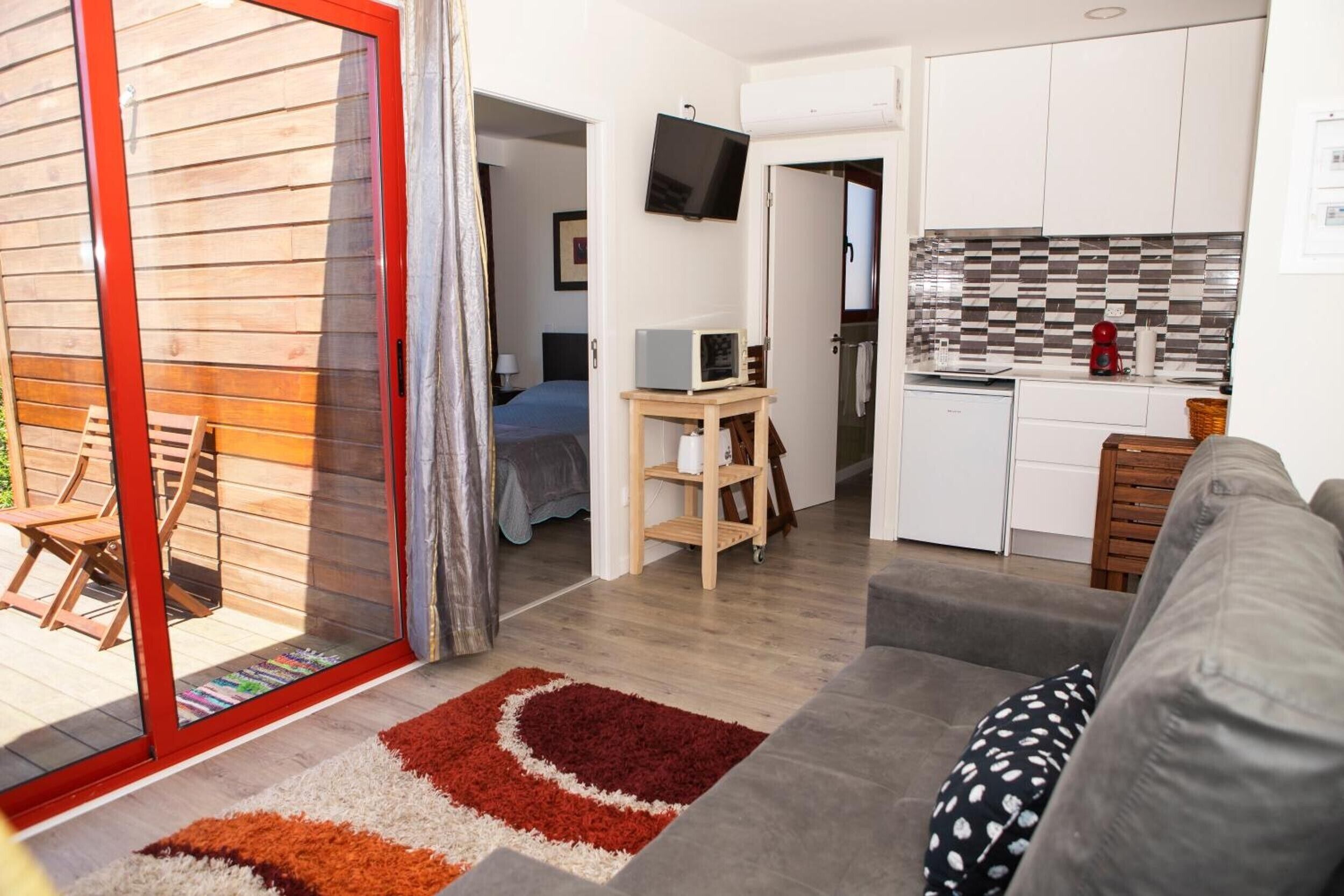A compact living space with a kitchenette, a sofa, a television, and a sliding glass door leading to an outdoor area.
