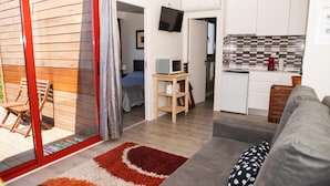 A compact living space with a kitchenette, a sofa, a television, and a sliding glass door leading to an outdoor area. - Bungalow 'Casinhas Do Minho' with Lake View, Wi-Fi and Air Conditioning (Ázere)