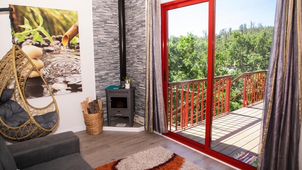 A cozy living room with a sofa, a hanging chair, a fireplace, and a balcony with a red railing. - Bungalow 'Casinhas Do Minho' with Lake View, Wi-Fi and Air Conditioning (Ázere)