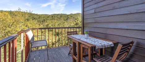 Terraza de madera con mesa y sillas, con vistas a una ladera boscosa.