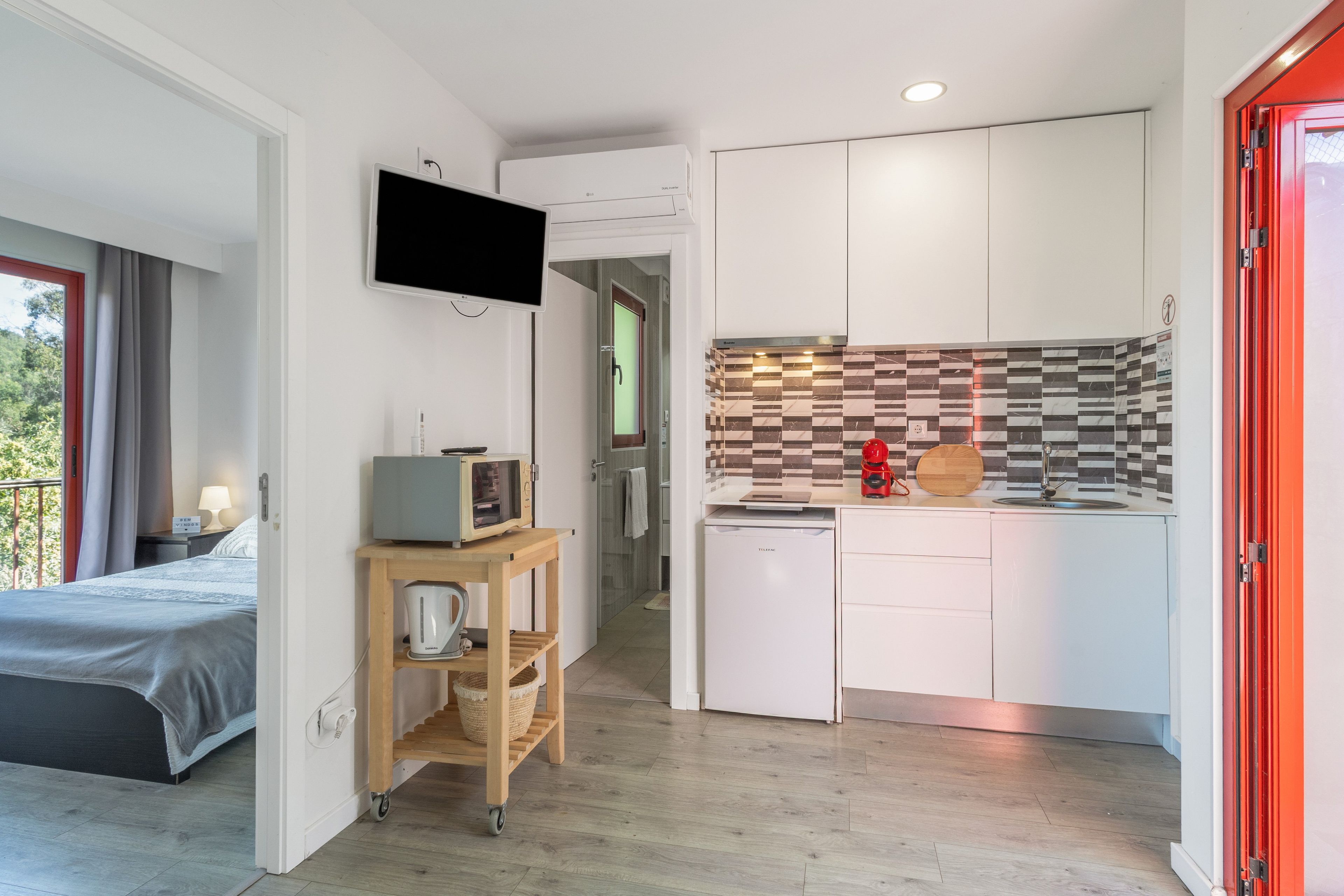 A compact hotel room with a kitchenette, a bed, a TV, and a small table with a microwave.