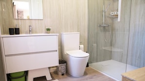A modern bathroom with a white vanity, toilet, and glass shower enclosure. - Bungalow 'Casinhas Do Minho' with Lake View, Wi-Fi and Air Conditioning (Ázere)