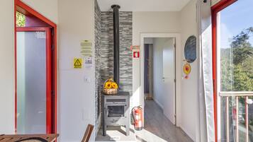 Una habitación con chimenea, una puerta con marco rojo, una pared con letrero de seguridad contra incendios y una ventana con vistas a árboles.
