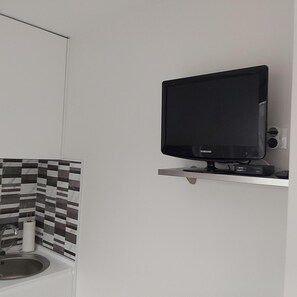 Un bagno con una TV Samsung nera montata a parete, una piastrella a mosaico e un lavabo con un rubinetto.
