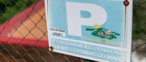 Ein Schild mit einem großen 'P', einem Standortmarker 'CASA DE PEDRA LUGAR 1' und einem privaten Parkbereich für 'ESTACIONAMENTO PRIVATIVO' für 'CLIENTES CASINHAS DO MINHO'.