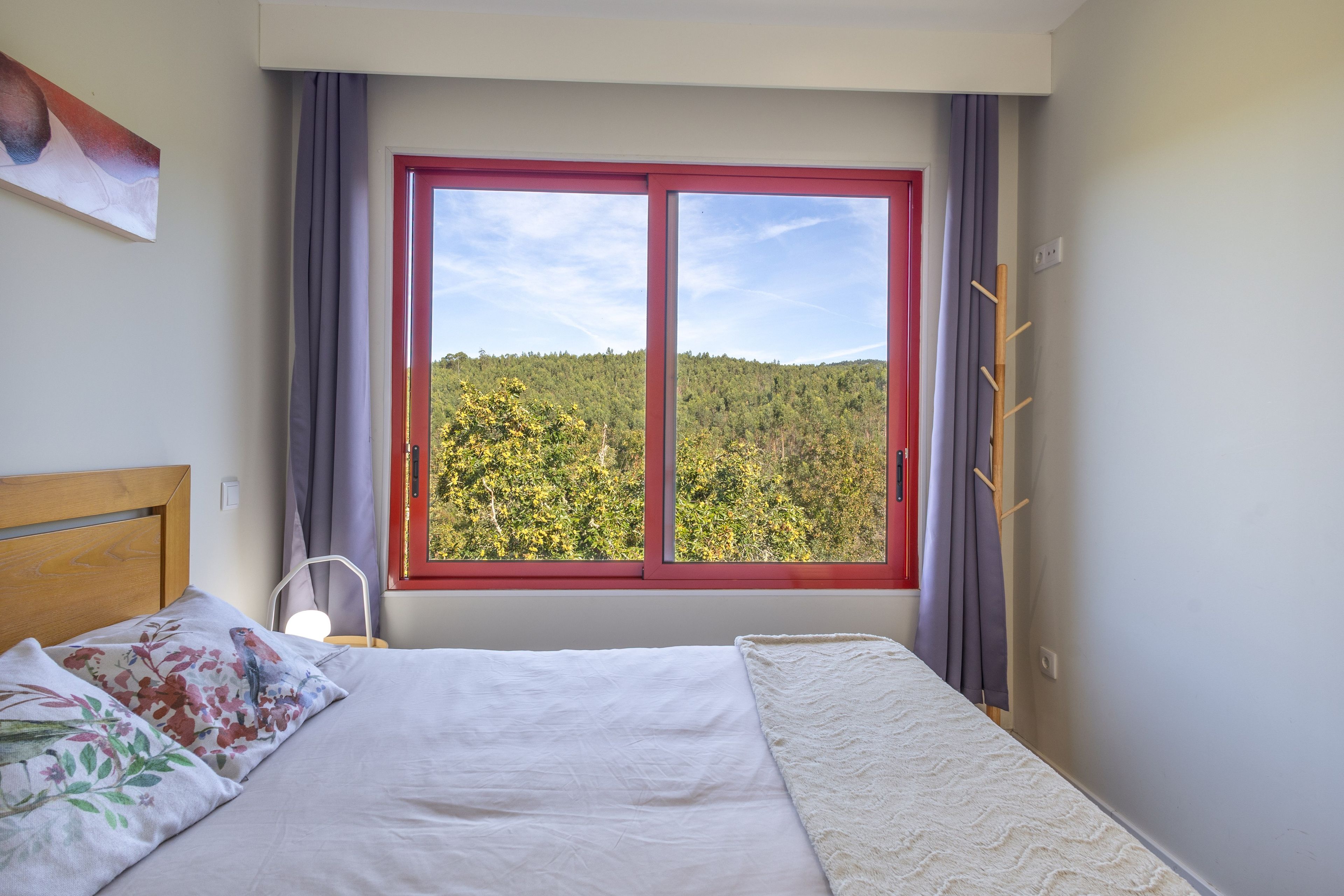 Ein Schlafzimmer mit einem Bett, einem Fenster mit Blick auf einen Wald und einem Kleiderständer.