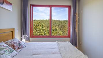 Une chambre à coucher avec un lit, une fenêtre donnant sur une forêt et un porte-manteau.