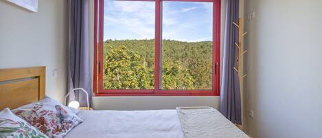 Ein Schlafzimmer mit einem Bett, einem Fenster mit Blick auf einen Wald und einem Kleiderständer.