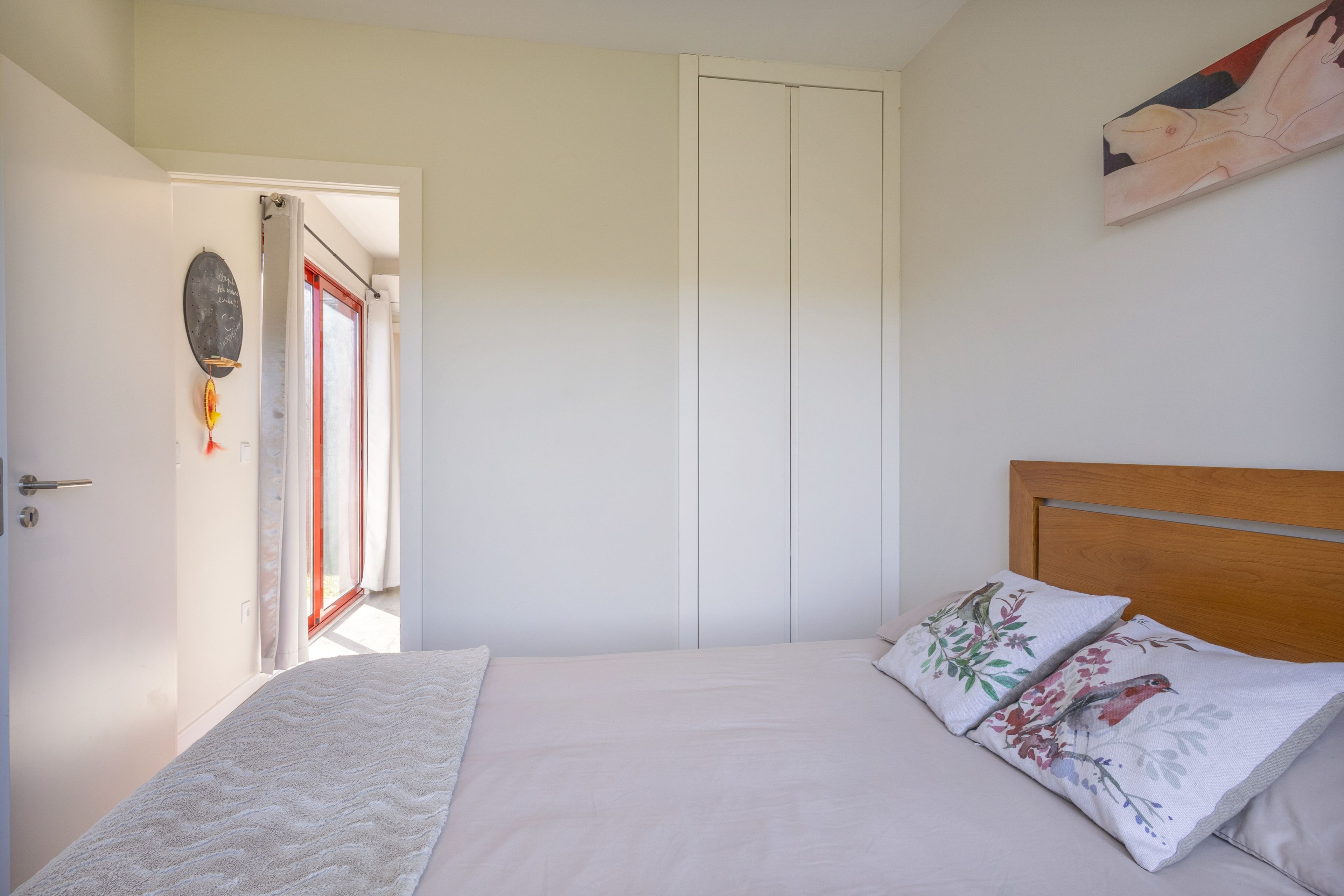 Un dormitorio con cama, almohadas, una puerta y una pared con un cuadro.