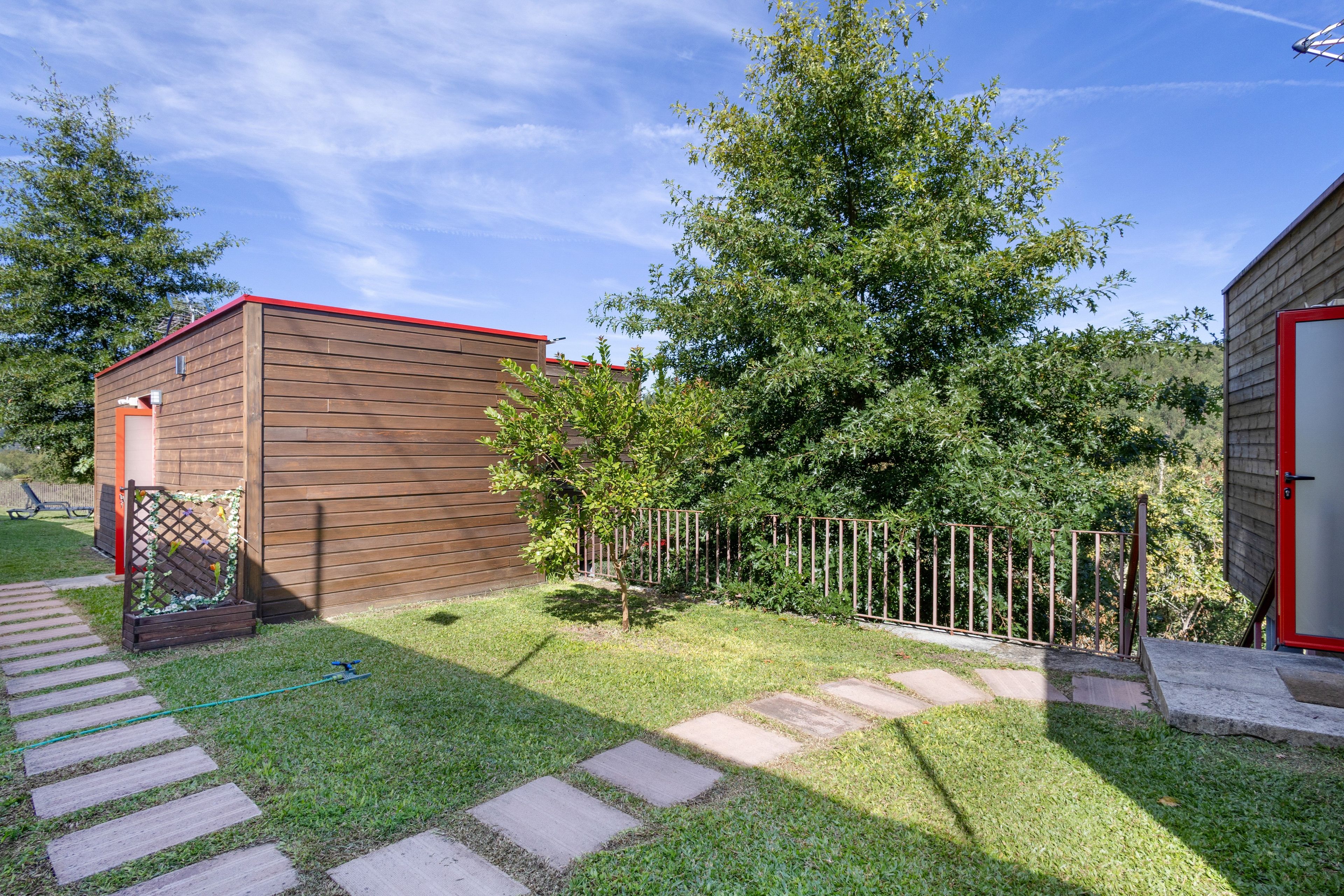 A wooden shed with a red roof, a metal fence, and a paved pathway leading to it.
