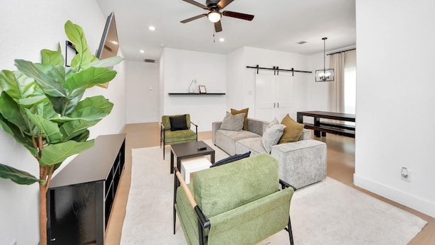 Un salon moderne comprenant un canapé, des fauteuils, une table basse, un téléviseur et un ventilateur de plafond.