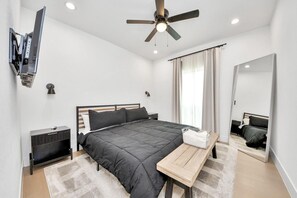 A modern bedroom with a bed, bedside table, TV mounted on the wall, ceiling fan, and a large mirror. - Modern 3BR NRG & Med center Downtown (Houston)