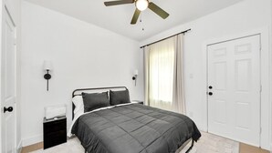 Une chambre à coucher avec un lit, un ventilateur de plafond, une table de chevet, une lampe et une porte.