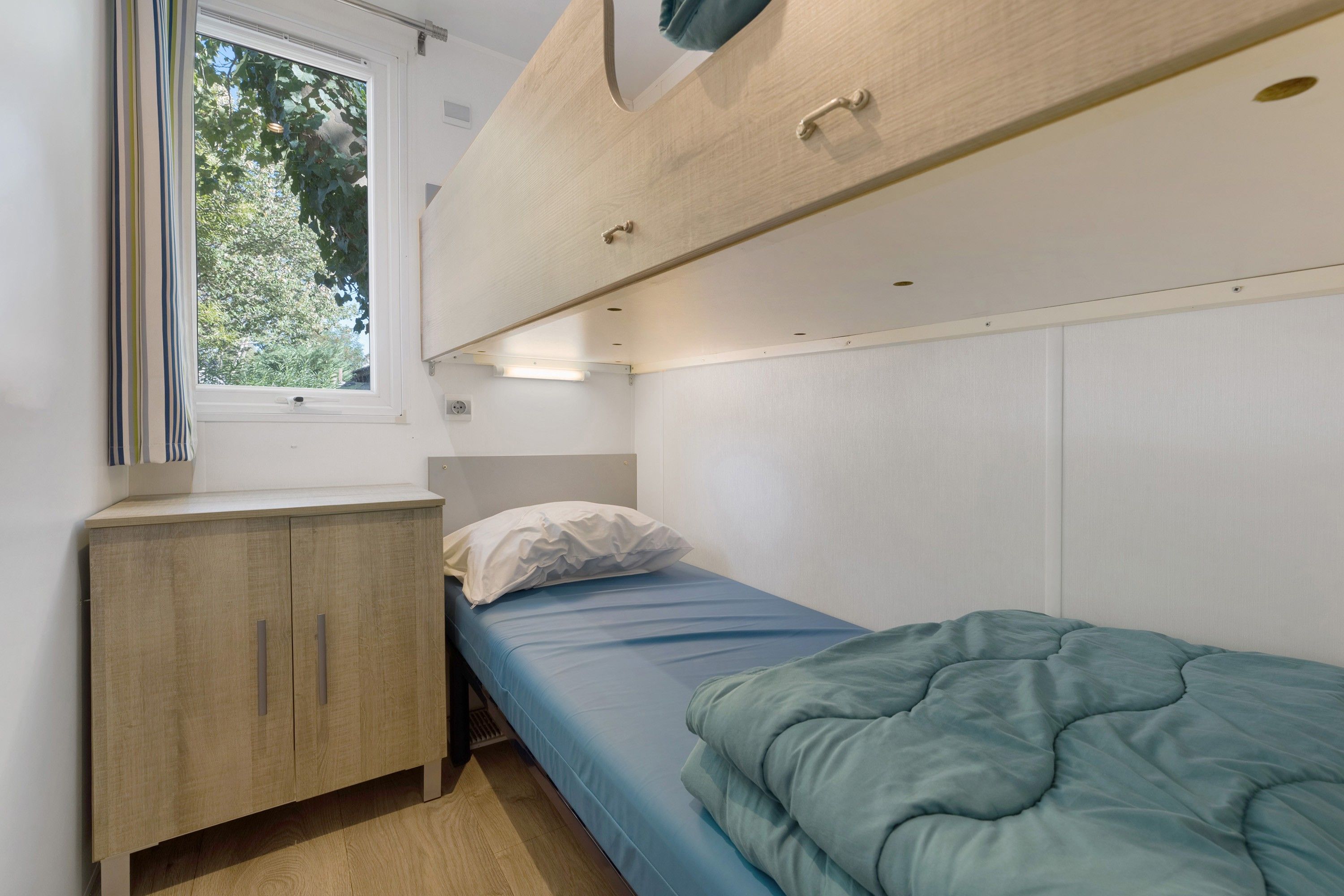 Una habitación pequeña con una cama individual, un archivador de madera y una ventana.
